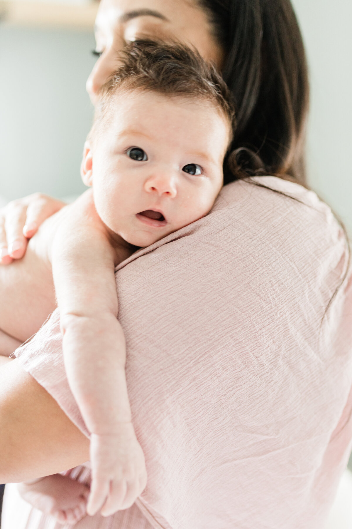 Mom wearing soft pink dress with infant daughter draped over her shoulder