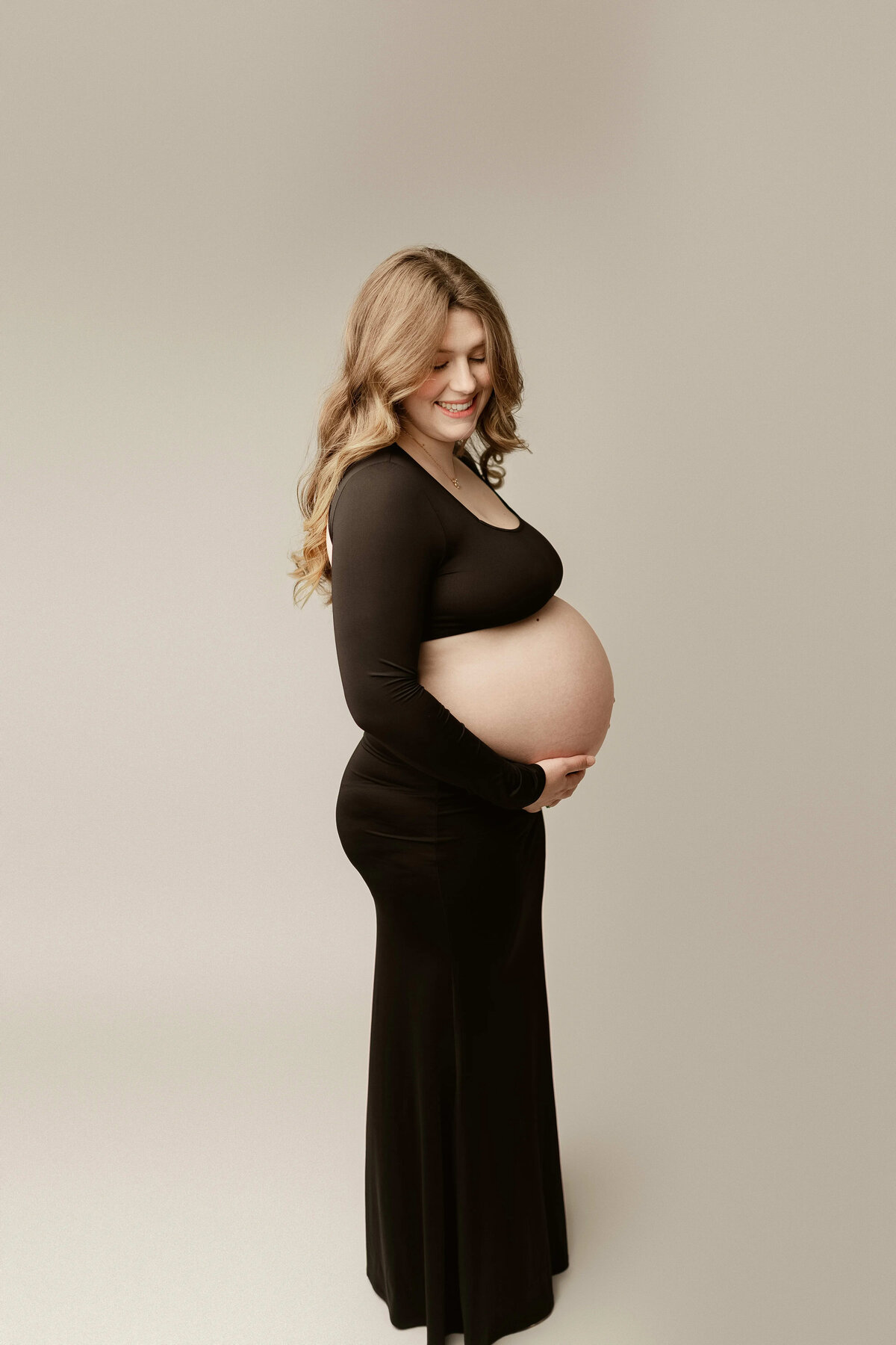 Side profile studio shot of smiling pregnant woman in black gown