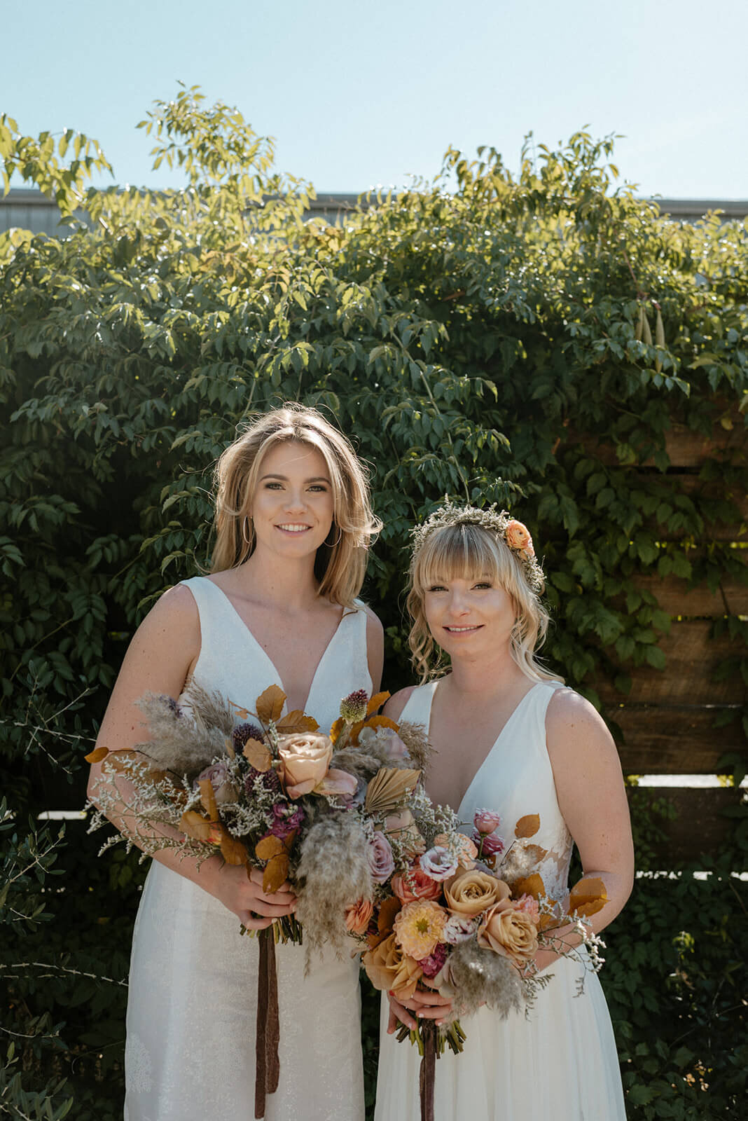 Boho-chic bridal inspiration featuring two brides with soft glam makeup, natural waves, and dried floral bouquets. Mistique Makeup offers wedding day hair and makeup for LGBTQ+ couples in Austin, Dallas, and San Antonio. Book our mobile makeup artist team for inclusive, on-location bridal services.
