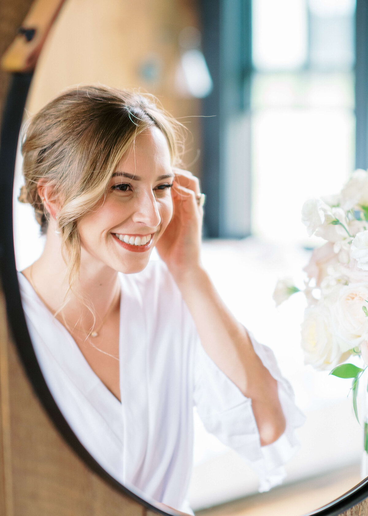 Lovely bride smiles at herself in the mirror while getting ready for her wedding ceremony