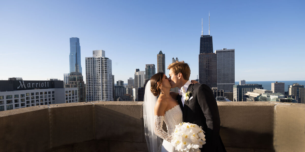 A bride and groom kissing in front of a city skyline