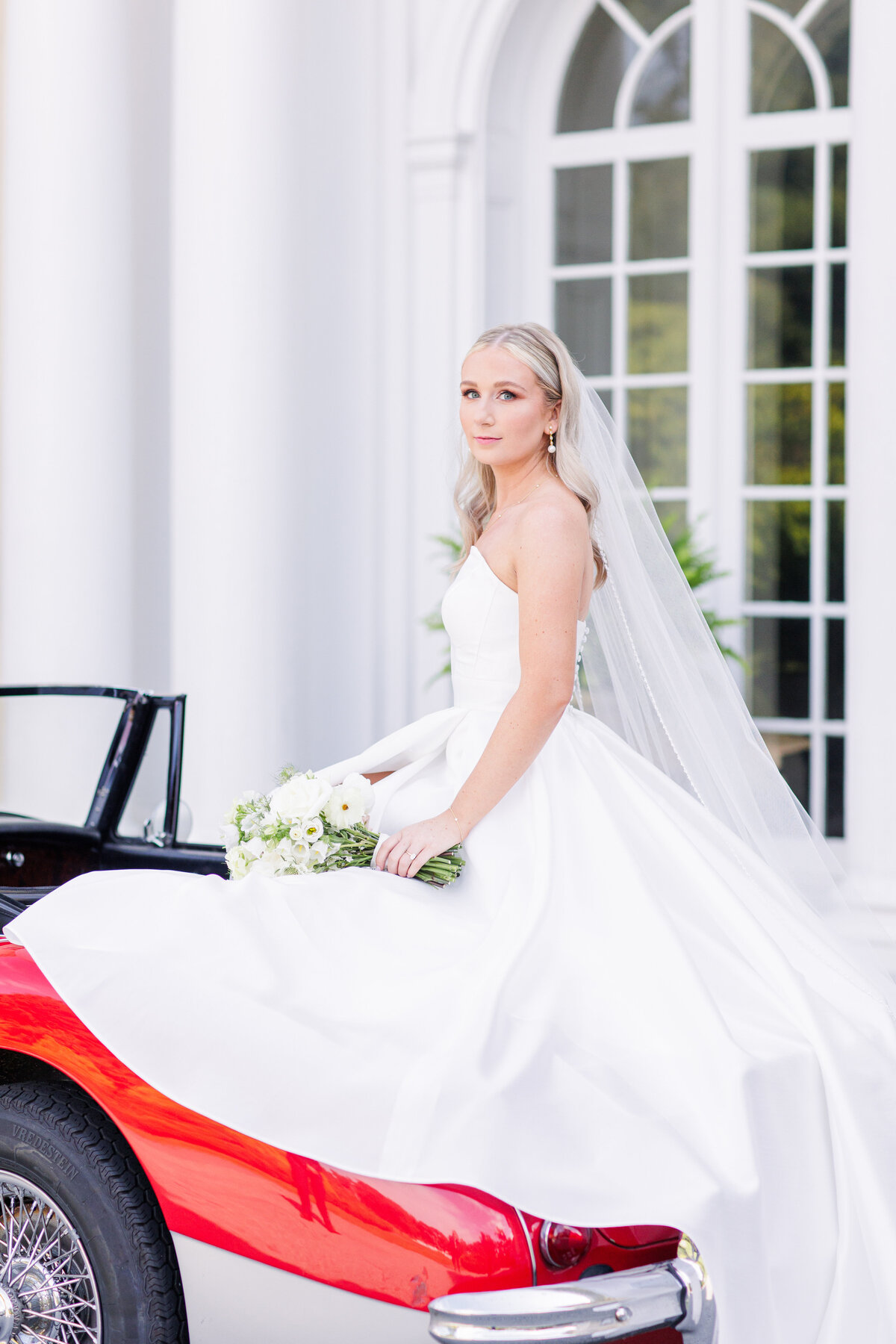 Bride sitting on a vintage car in front of Tupper Manor representing editorial Boston wedding photography