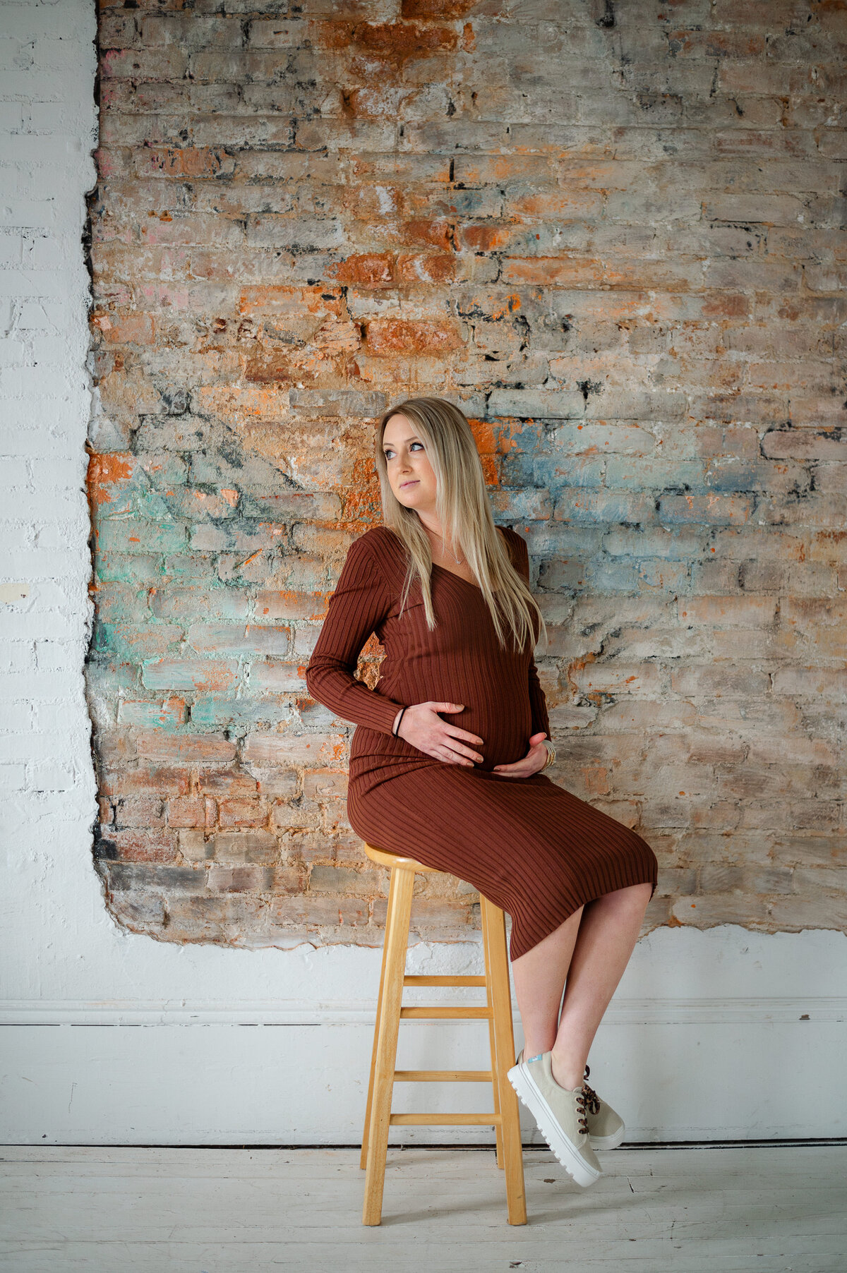 Pregnant mother sits on stool in front of beautiful exposed brick at Relic 15 Studio in Buford, GA