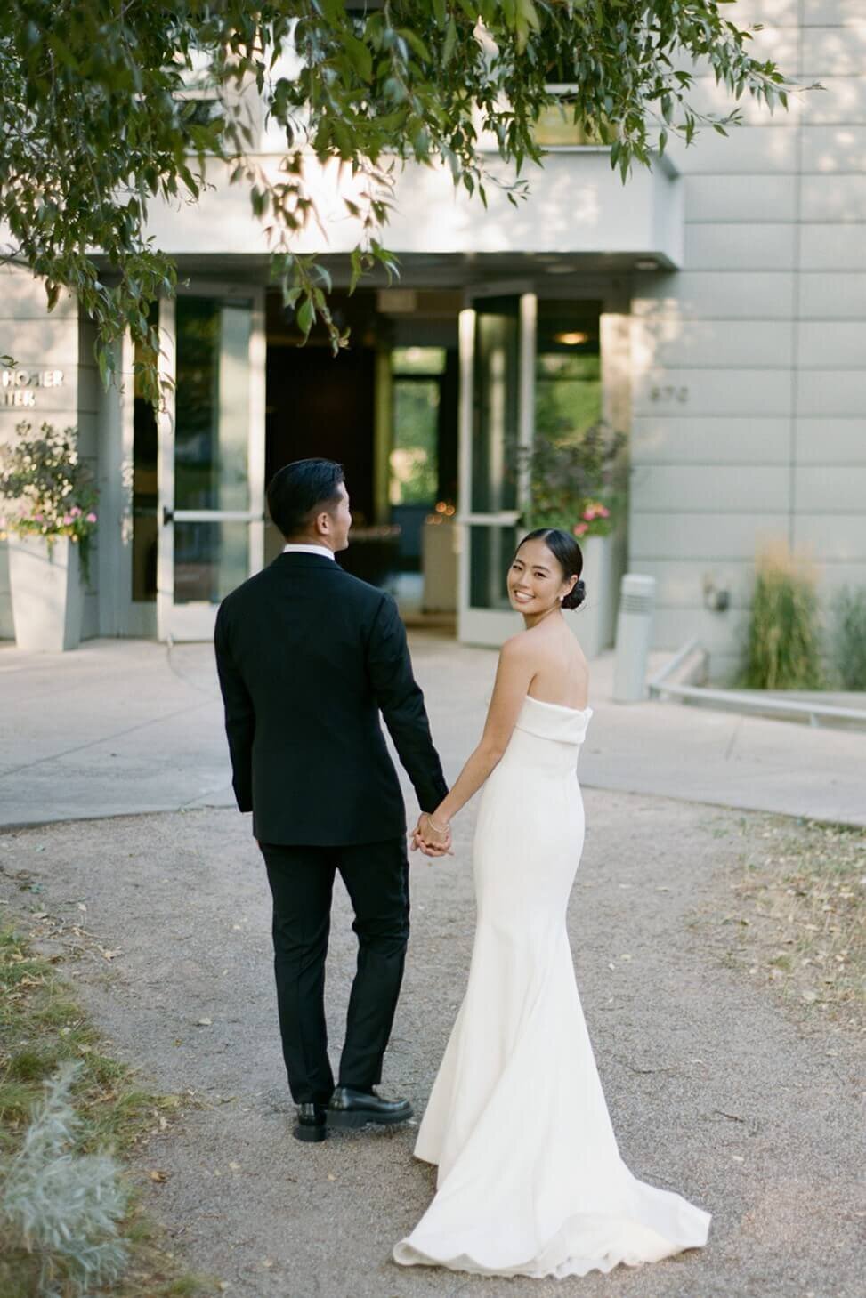 Bride looks over the shoulder and smiles while she and the groom walk under the beautiful greenery at the Aspen Meadows Resort wedding reception venue.