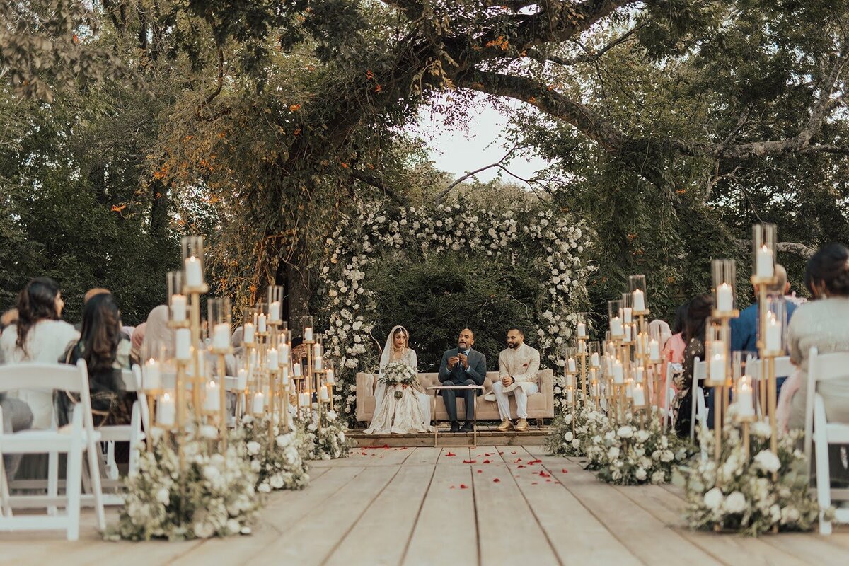 Ceremony backdrop filled with white flowers, greenery, and gold multi leveled candles at the Bowery House and Gardens.