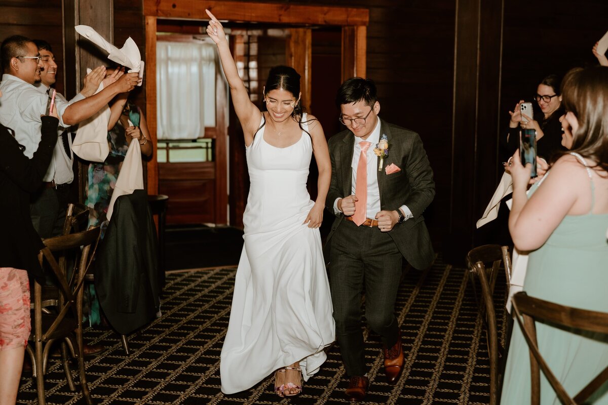 Bride and groom make a joyful grand entrance into their wedding reception at Hollow Brook Golf Club, surrounded by cheering guests and waving napkins.