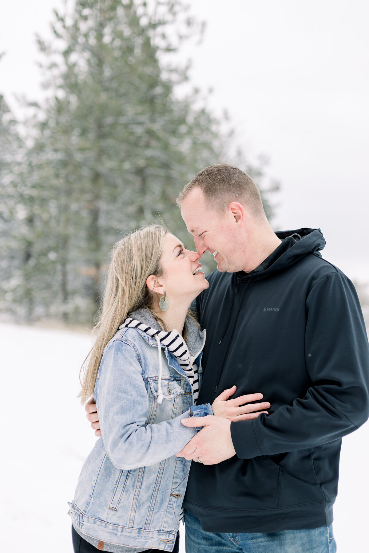 Mom and dad smiling and looking at each other in the cold snow taken by spokane family photographer