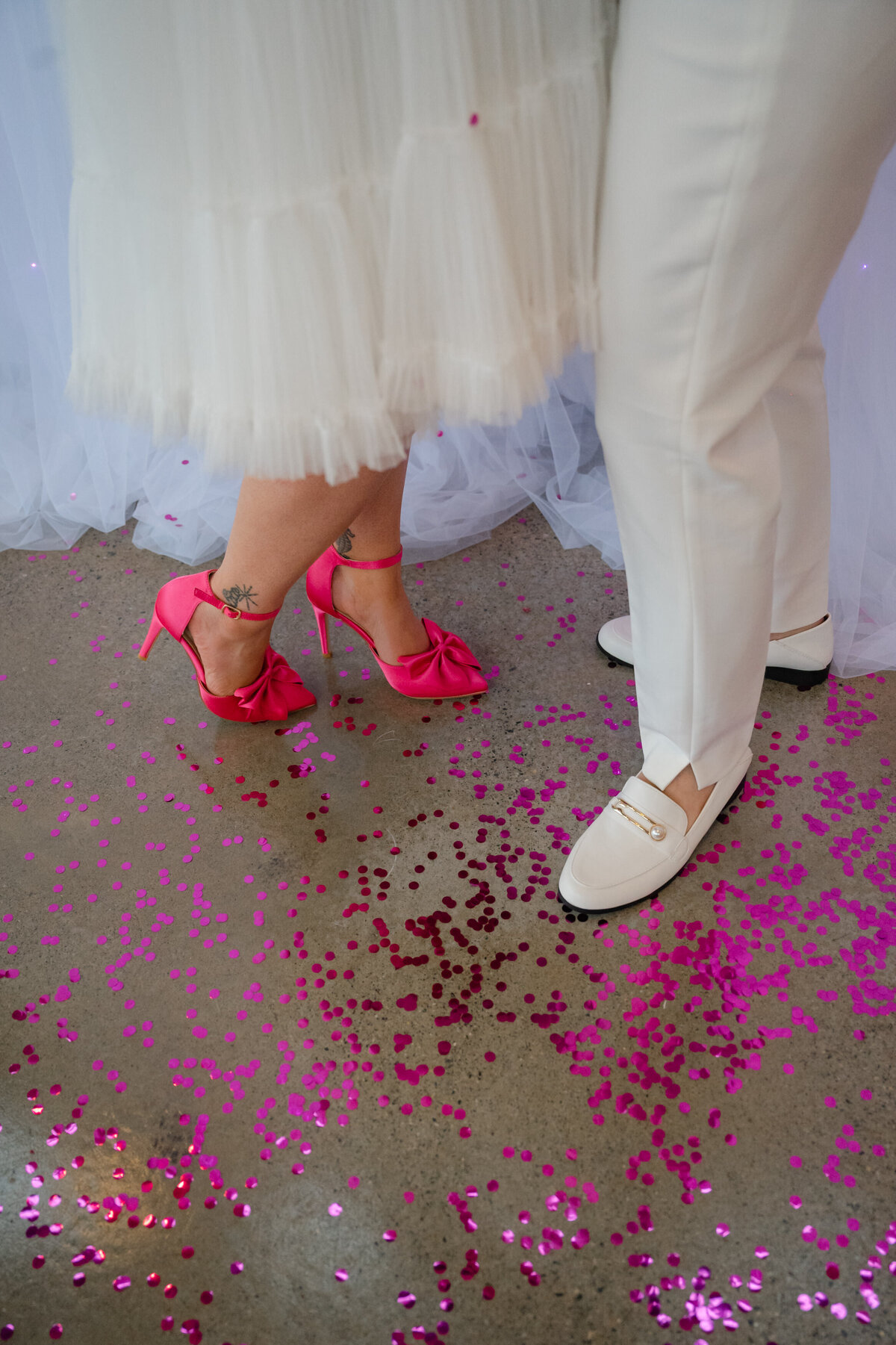 Wedding shoe closeup. The brides are wearing white loafers and hot pink heels.