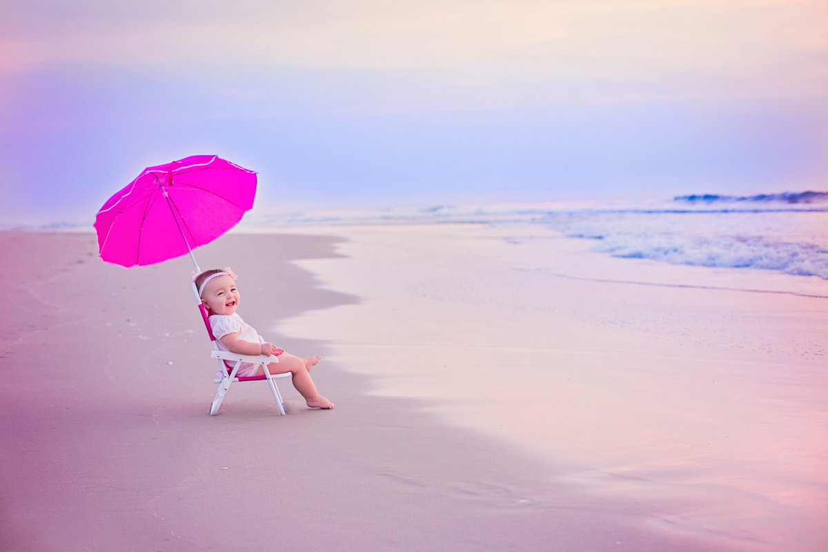 charlotte family photographer jamie lucido creates gorgeous image of child sitting on a chair with an umbrella at Outer Banks, north carolina shore