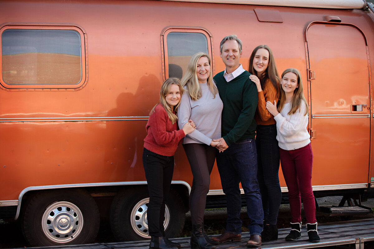 Warm autumn family photo in front of orange metallic van, parents and three girls in colorful sweaters at Camp North End Charlotte NC