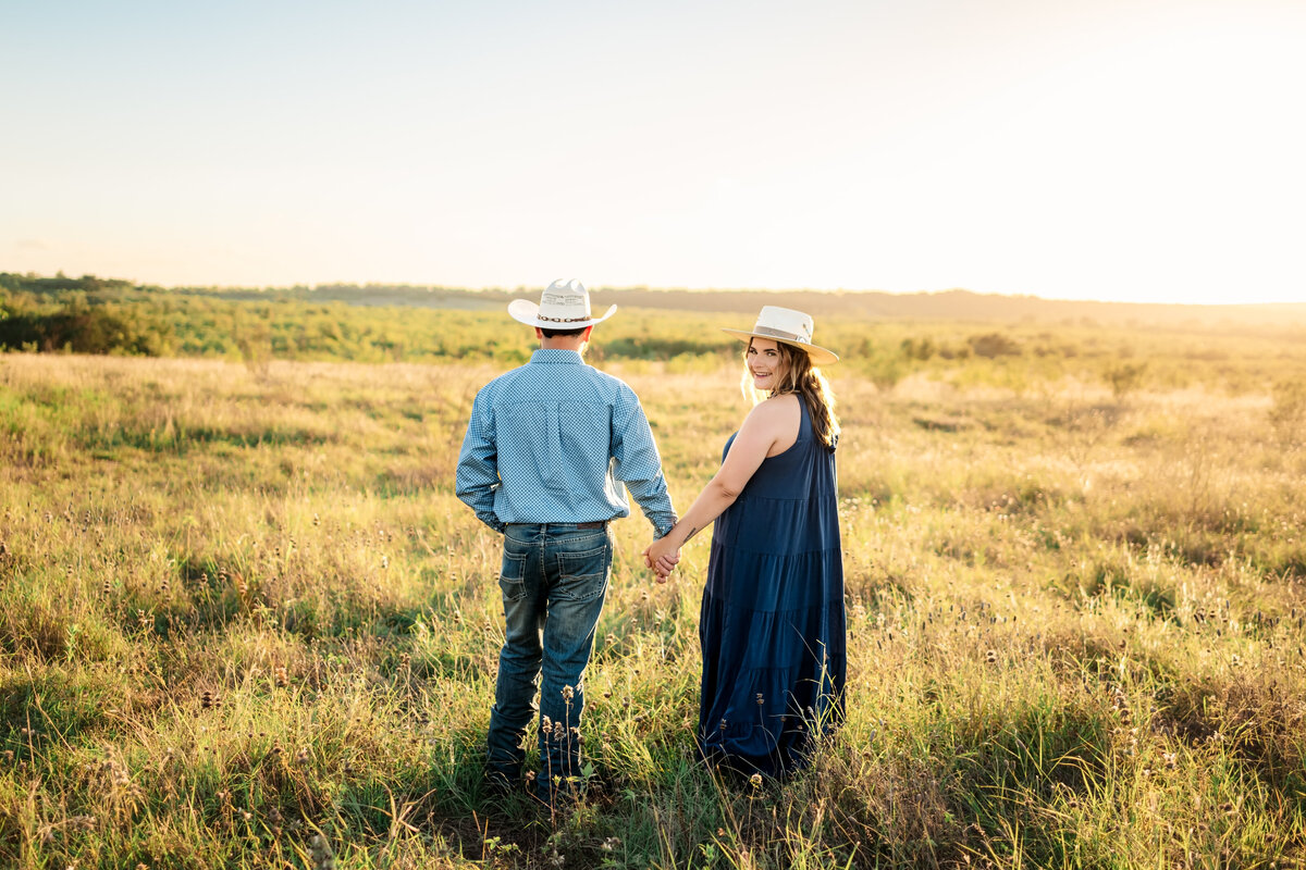 Engaged couple standing in open field during sunset engagement session at Harper Hills in New Braunfels, Texas.