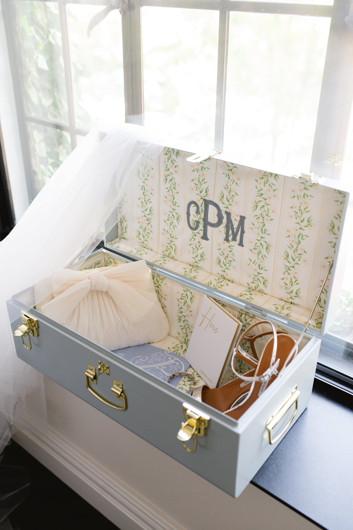 Wedding accessories in a decorative suitcase by a window.