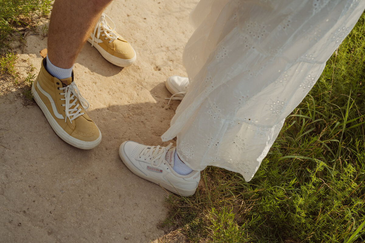 A close-up detail shot of the couple’s feet as they face each other on a sunlit path in the park near White Rock Lake.