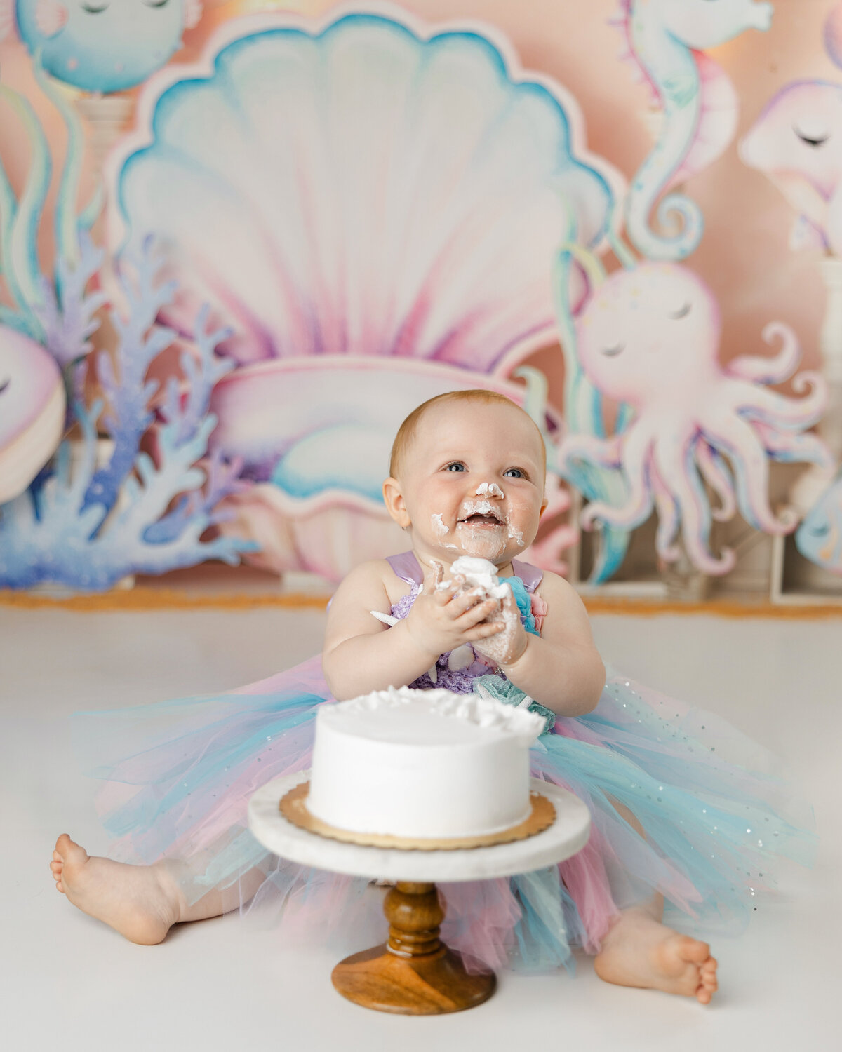 Baby enjoying a cake smash in a pastel mermaid-themed setup. Photograph by Yucaipa cake smash photographer Kaitlyn Dawn Photography.