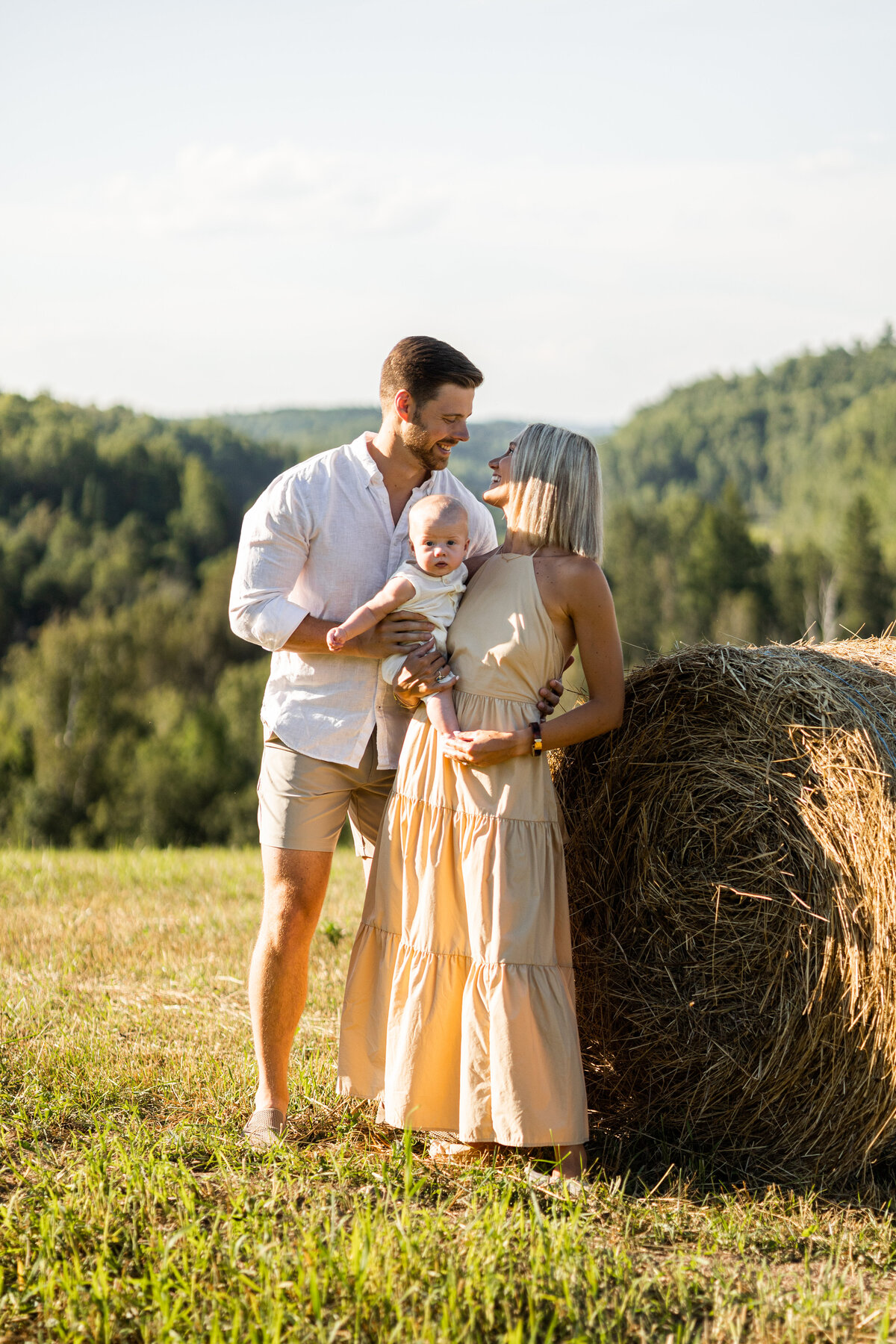 Couple holding their 6 month old baby in a field in Val-des-monts at their cottage