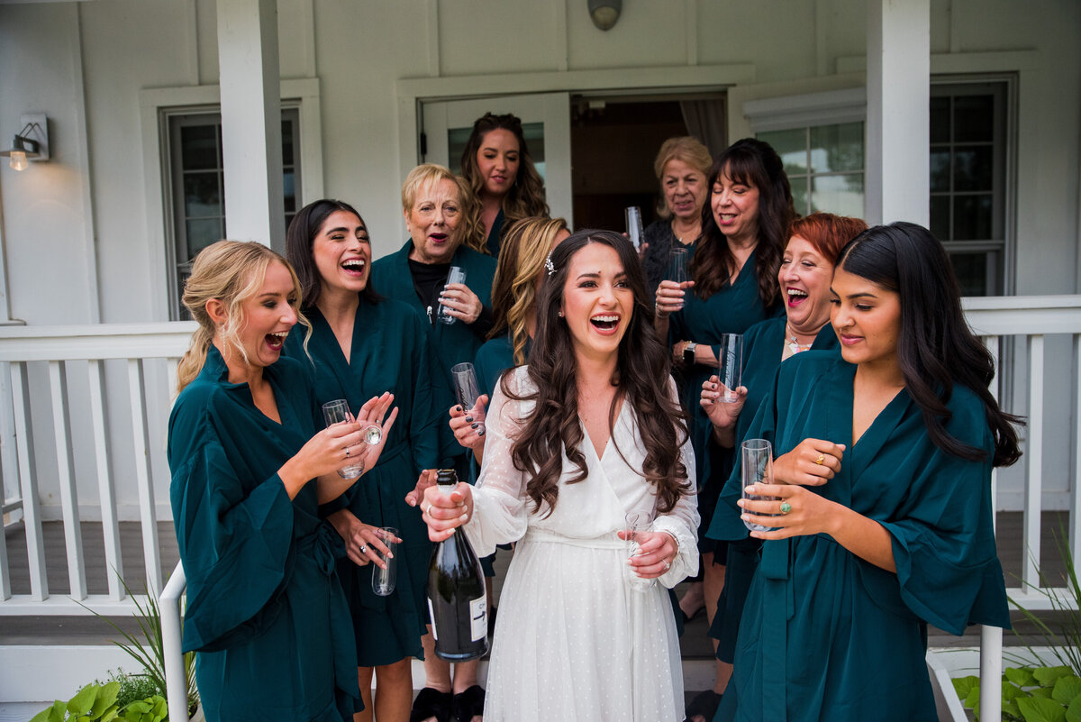 A bride and her bridesmaids wearing robes share glasses of champagne in front of the cottage at The Barn at Raccoon Creek in Colorado.