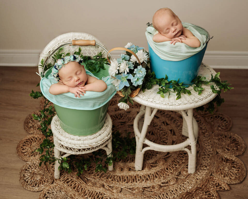 Boy and girl newborn twins posed beside eachother in buckets at their toronto newborn photographer studio on little table and chair with greenery.