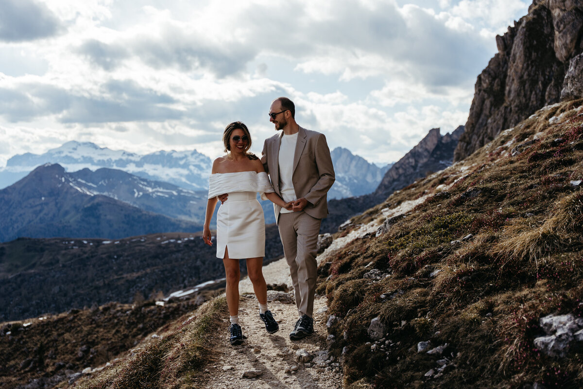 Couple walking across meadow surrounded by rocky peaks