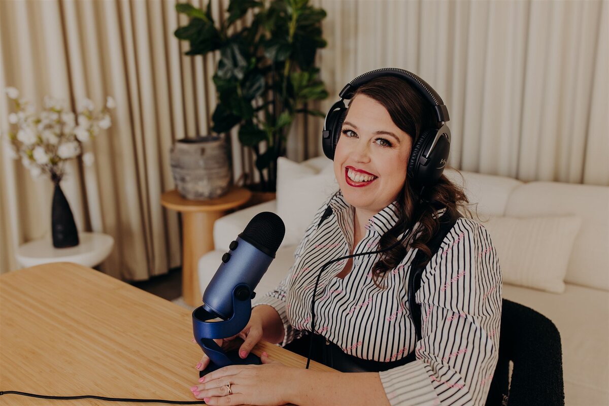 sex therapist sitting at desk in striped shirt while holding a podcast mic