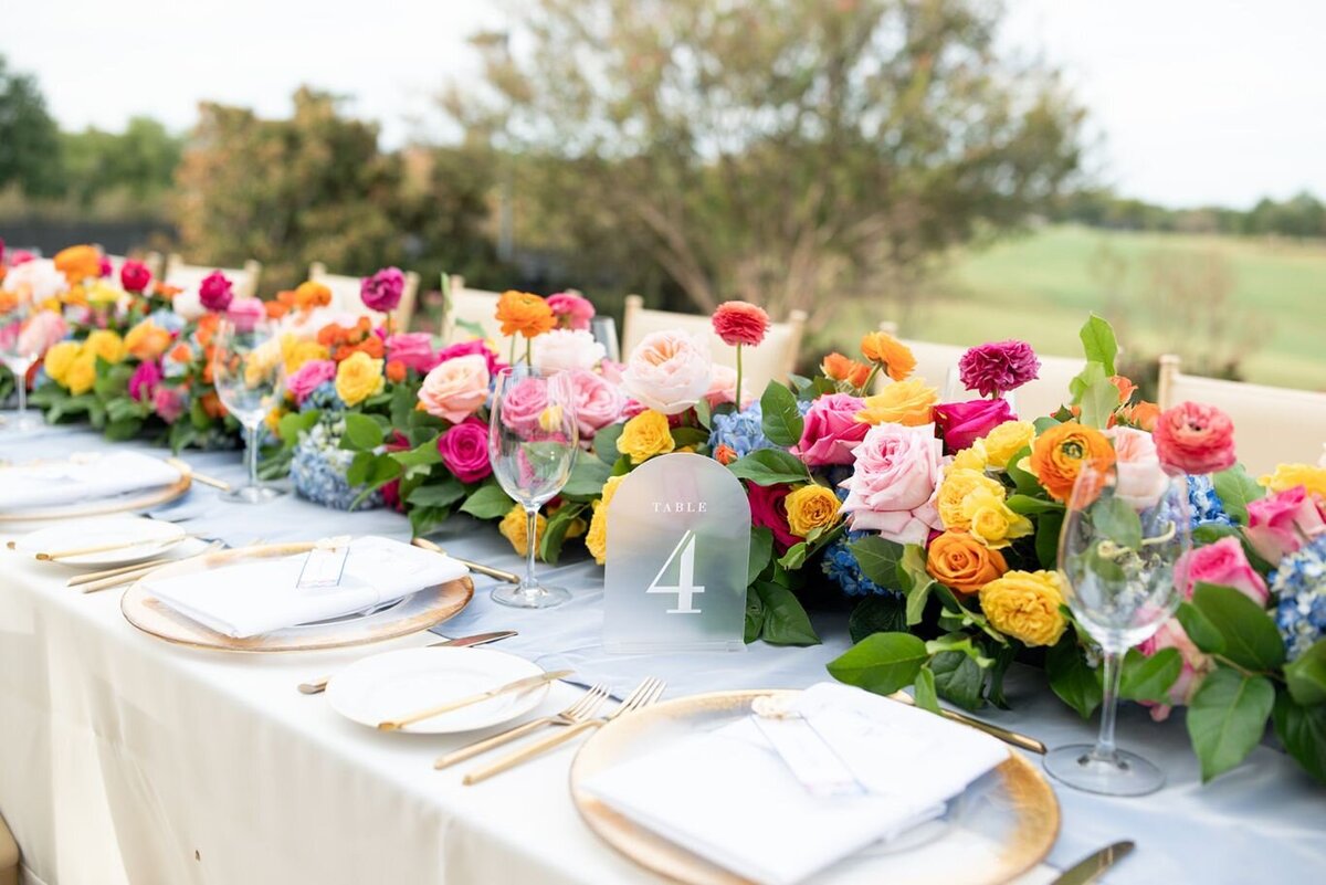 Colorful garden-inspired wedding floral centerpiece with vibrant roses, ranunculus, and fresh greenery at outdoor reception