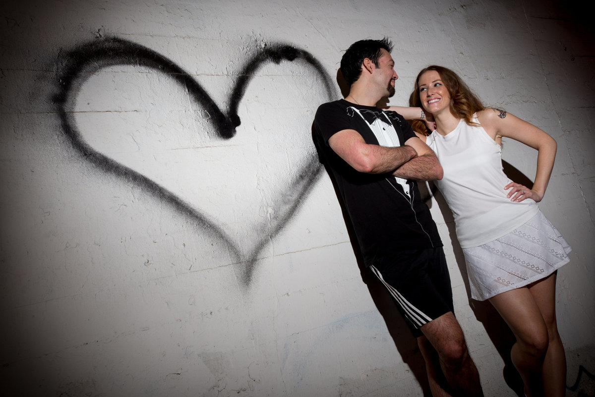 Engagement couple with black spray painted heart on the wall