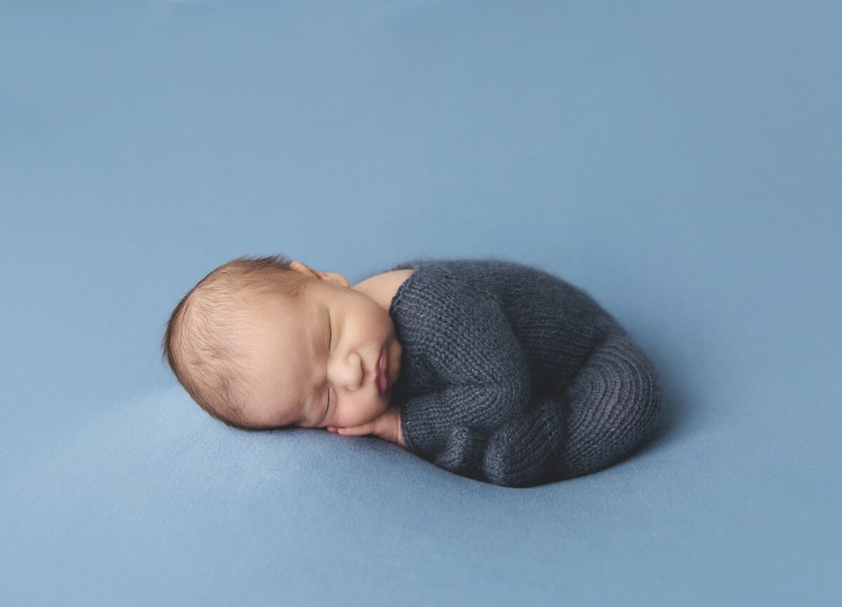 Newborn curled up in knit blue swaddle