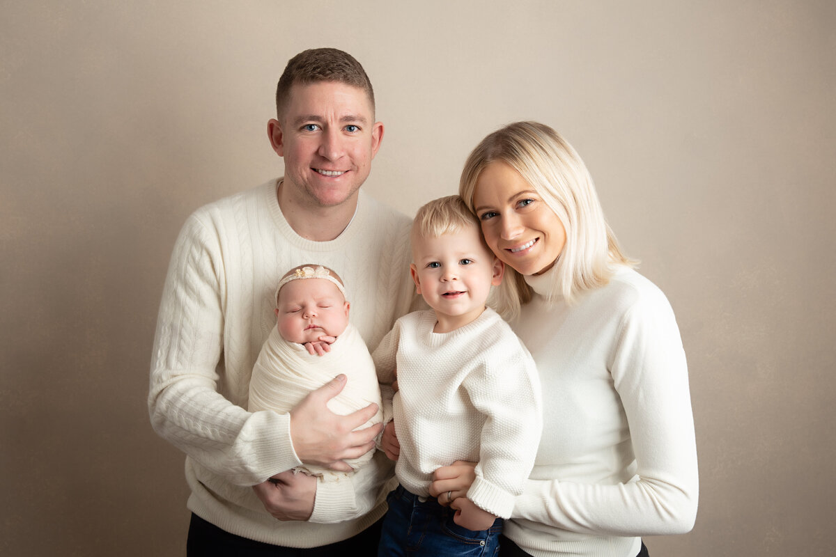 Family of four with a newborn and toddler  all wearing cream on a cream background.