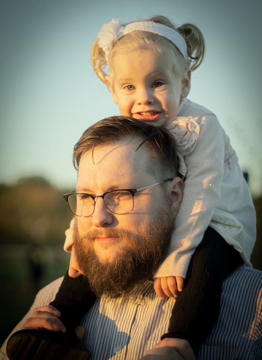 closeup of a dad with glasses with his little girl on his shoulders