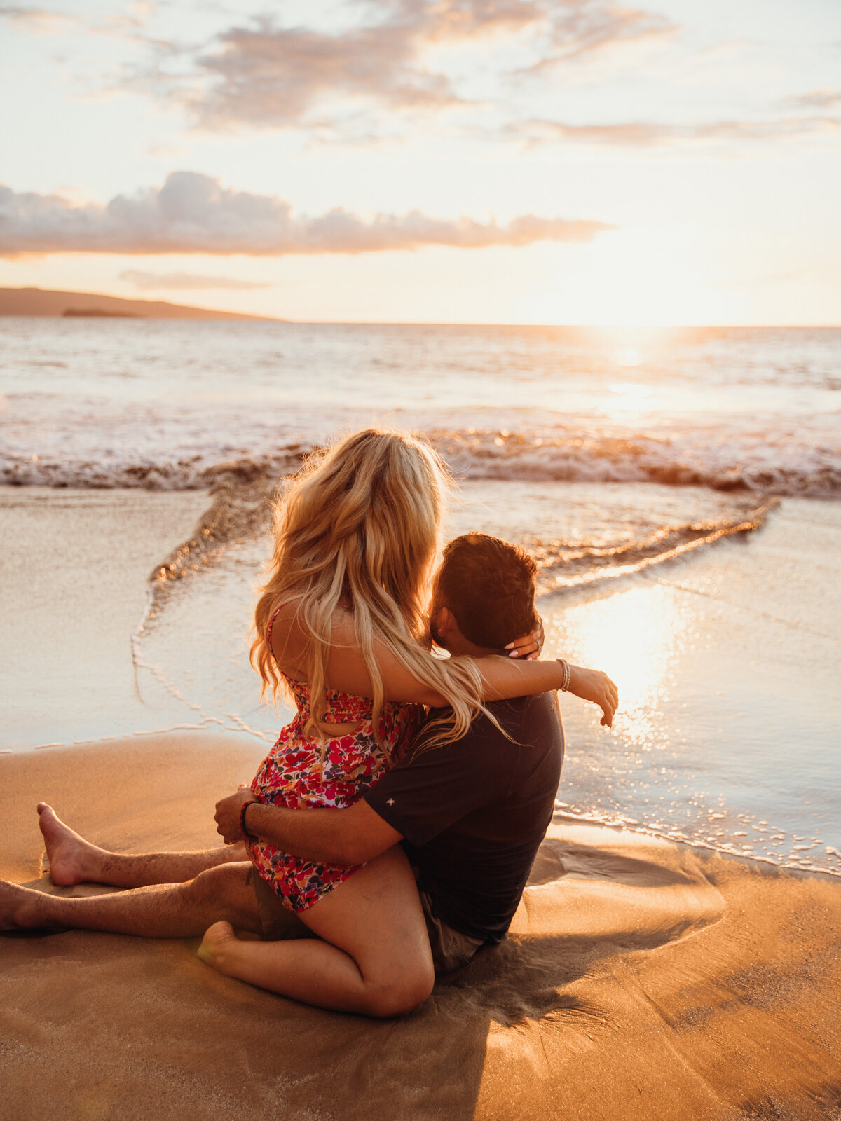 Hawaii Engagement Photographer captures woman sitting on man's lap during engagement photos on beach