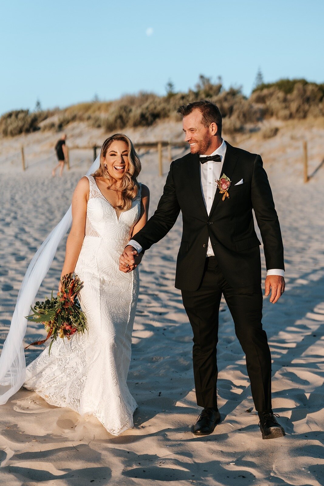 A bride and groom laughing while walking along the beach