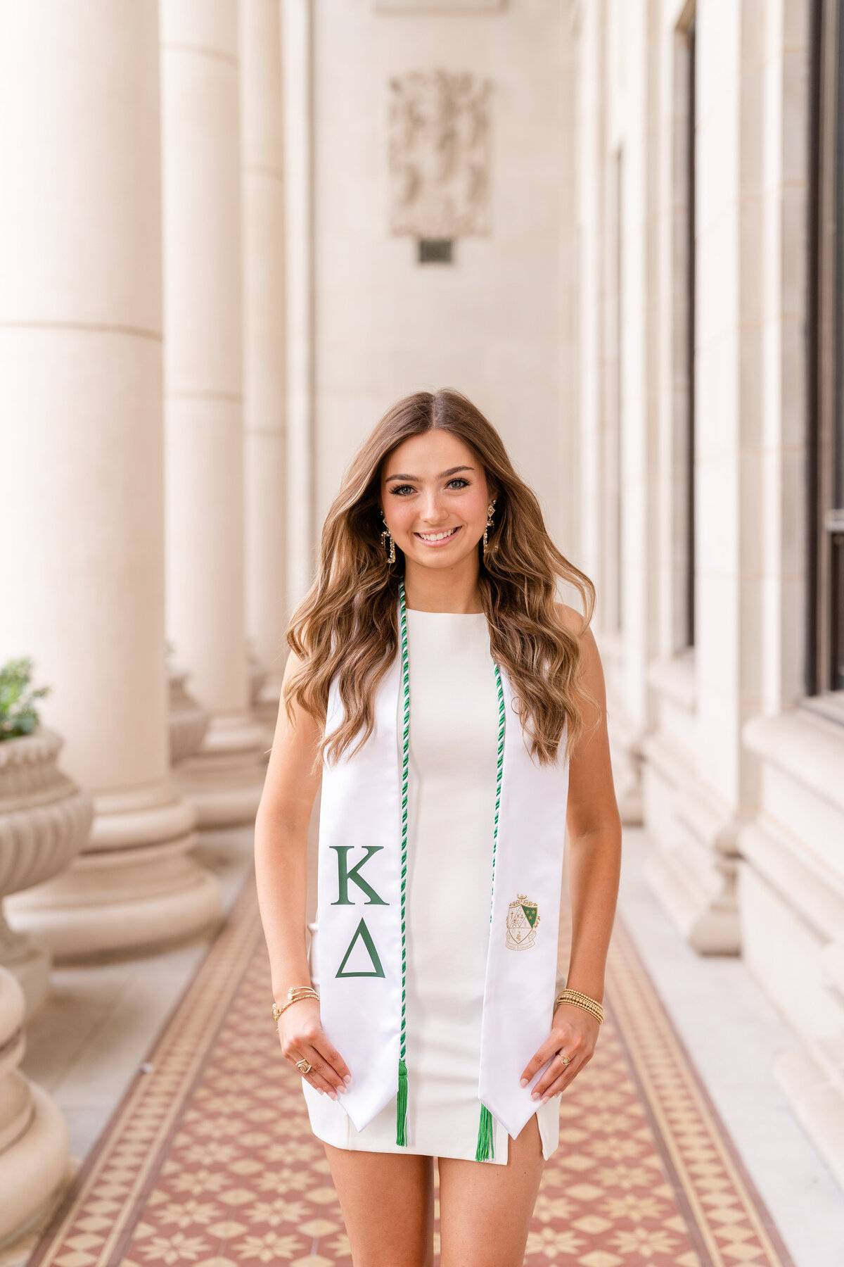 Texas A&M senior girl smiling and holding Kappa Delta stole and white dress in columns of Administration Building