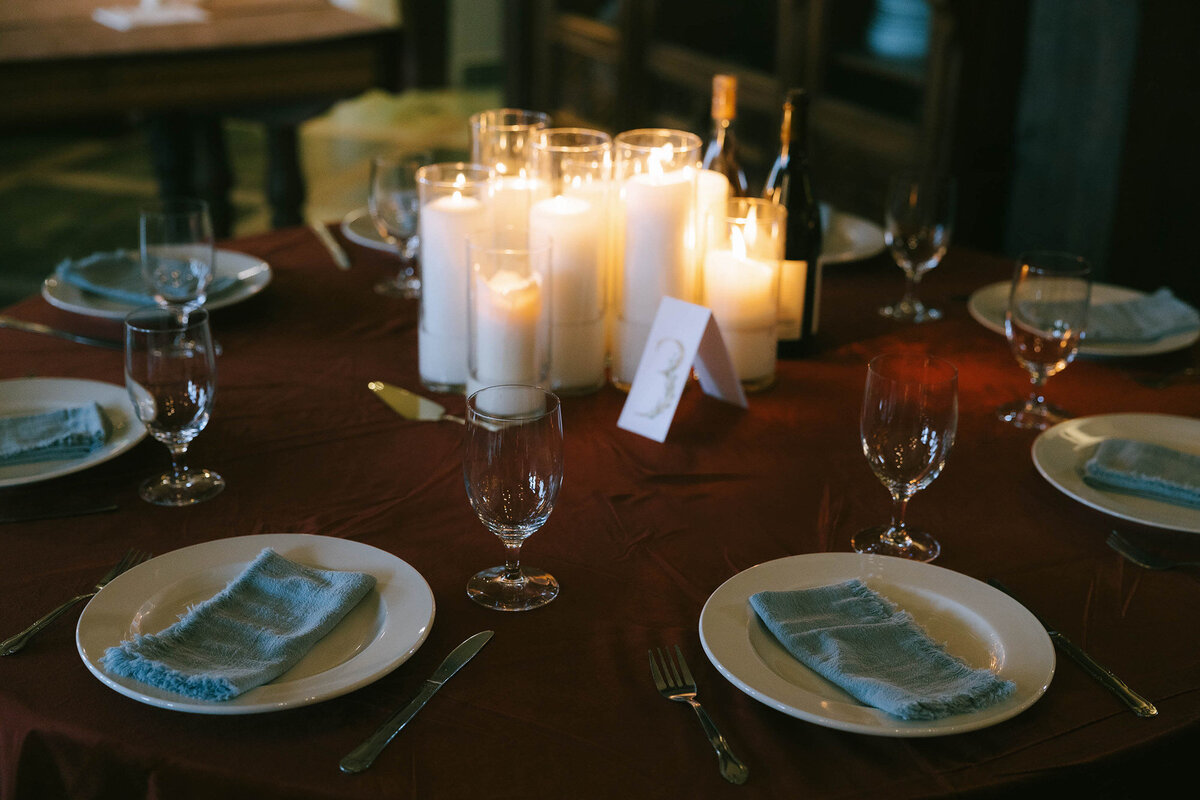 Lit candles in the middle of a table set at an indoor wedding reception at the Chateau De Lis.
