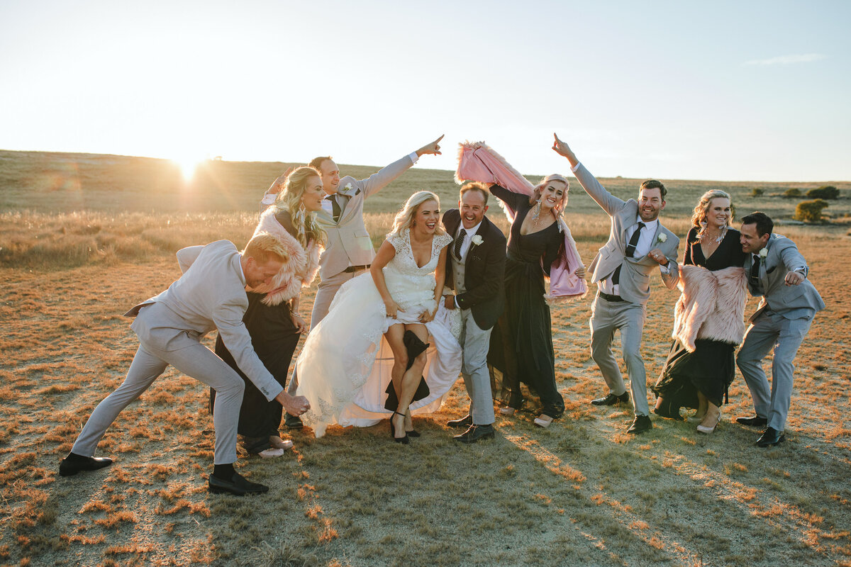 Bridal party laughing and having fun together as the sun sets behind them, captured in a spontaneous, documentary-style moment.