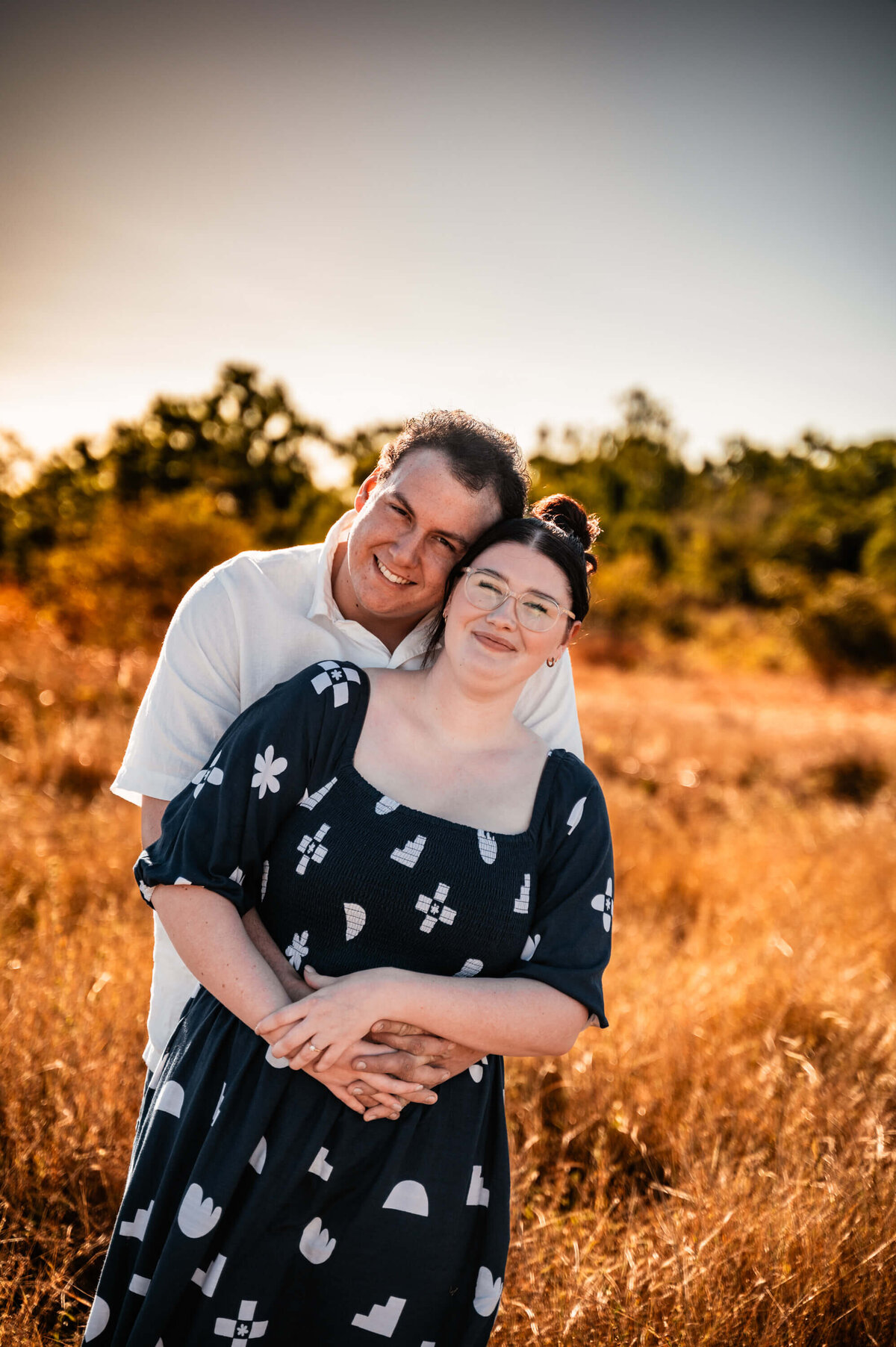 A couple stands together in a field, silhouetted against a vibrant sunset, capturing a moment of intimacy and tranquility. - photo by Jamie SImmons