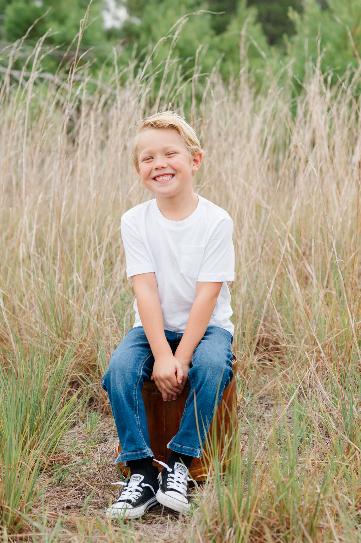Young blonde boy sitting on a bucket and smiling at the camera