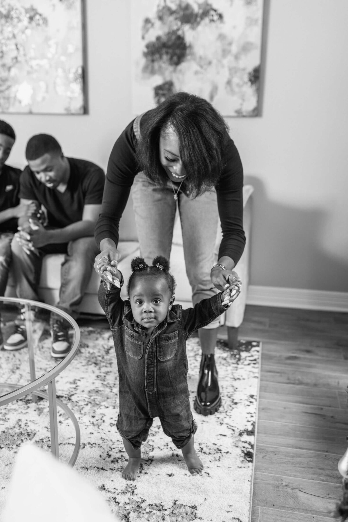 candid black and white photo of mom helping infant walk in living room during in home lifestyle family photography session