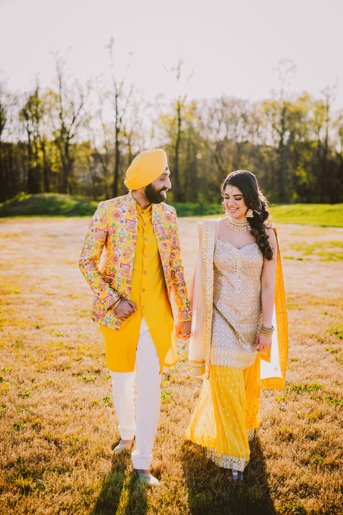 Sikh bride and groom walking outside on grass at their sangeet jaago in yellow outfits