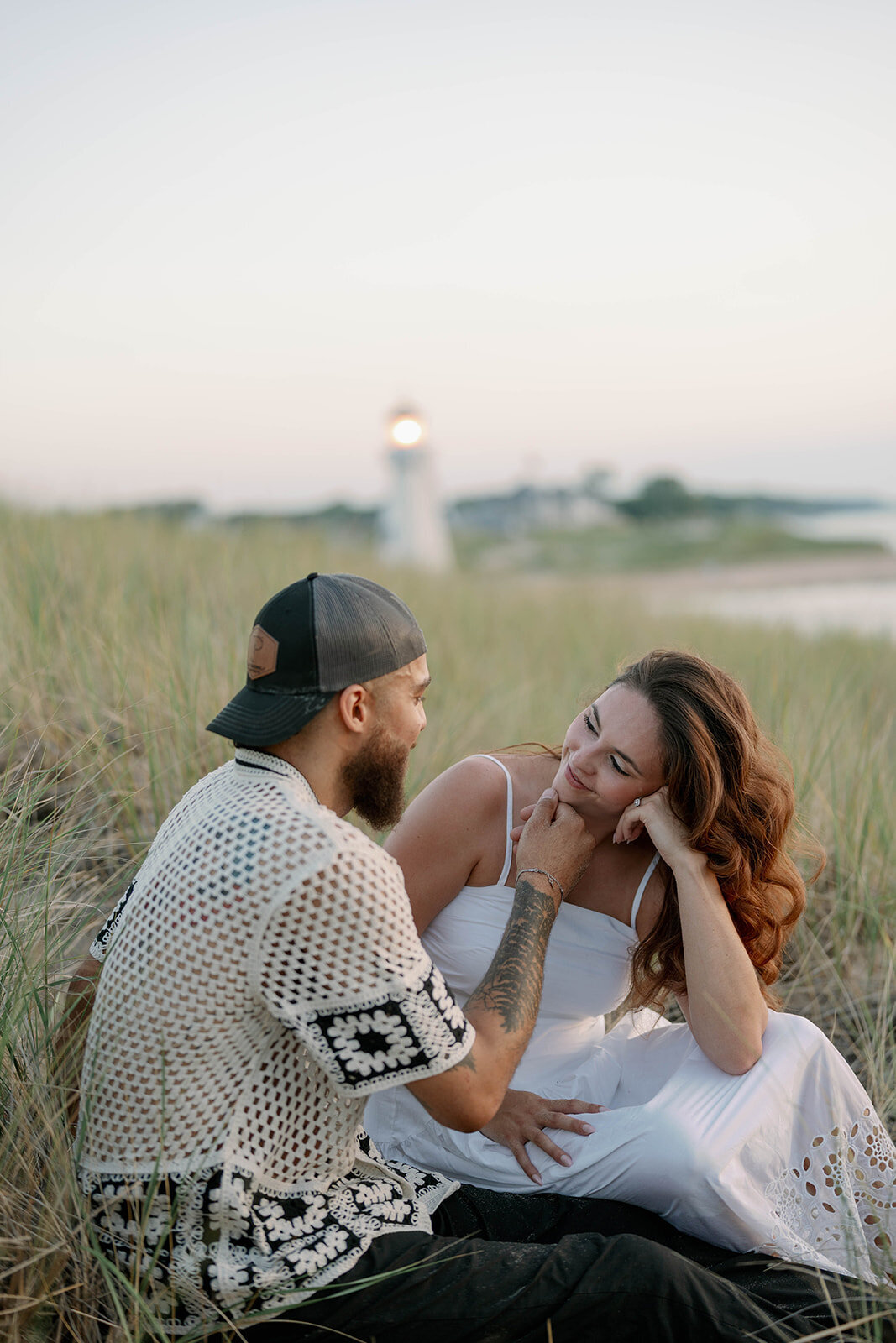Couple sitting in beach grass during their Lake Michigan engagement session at New Buffalo Beach at sunset