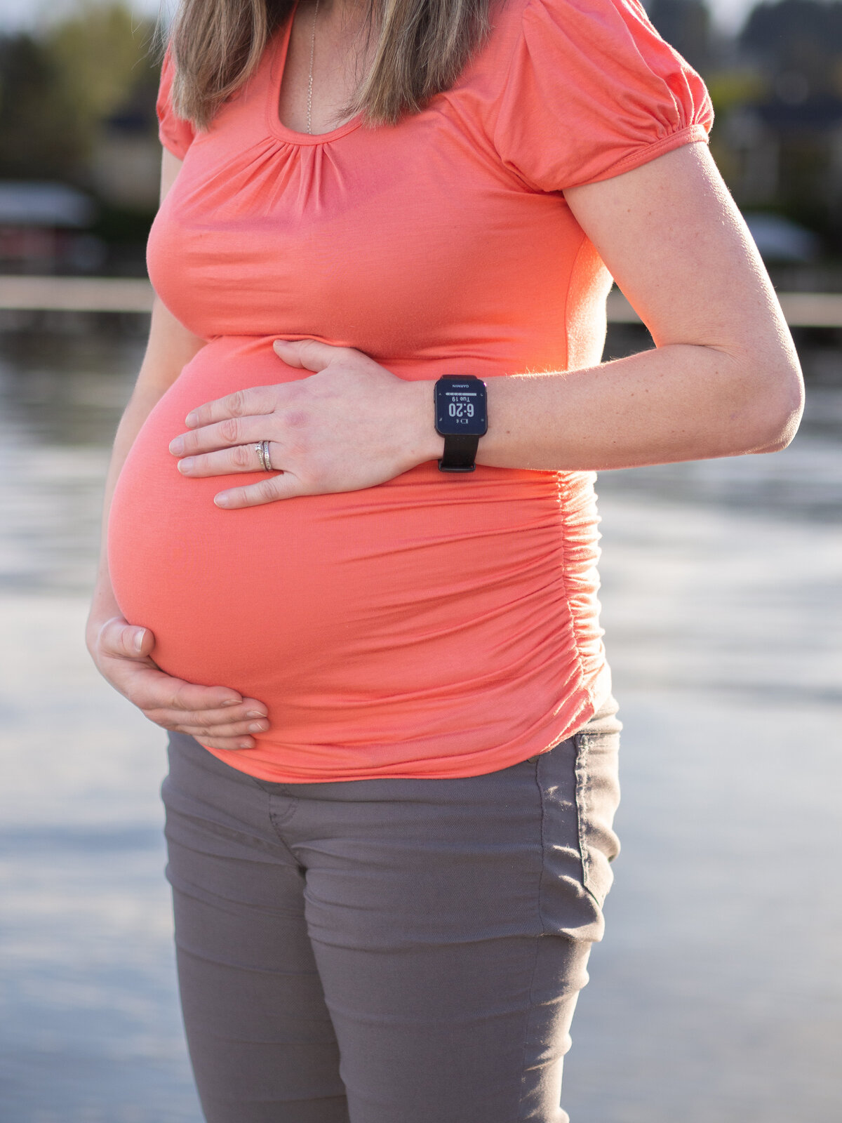a pregnant woman holds her pregnant belly while she stands along Lake Washington in Kenmore, WA.