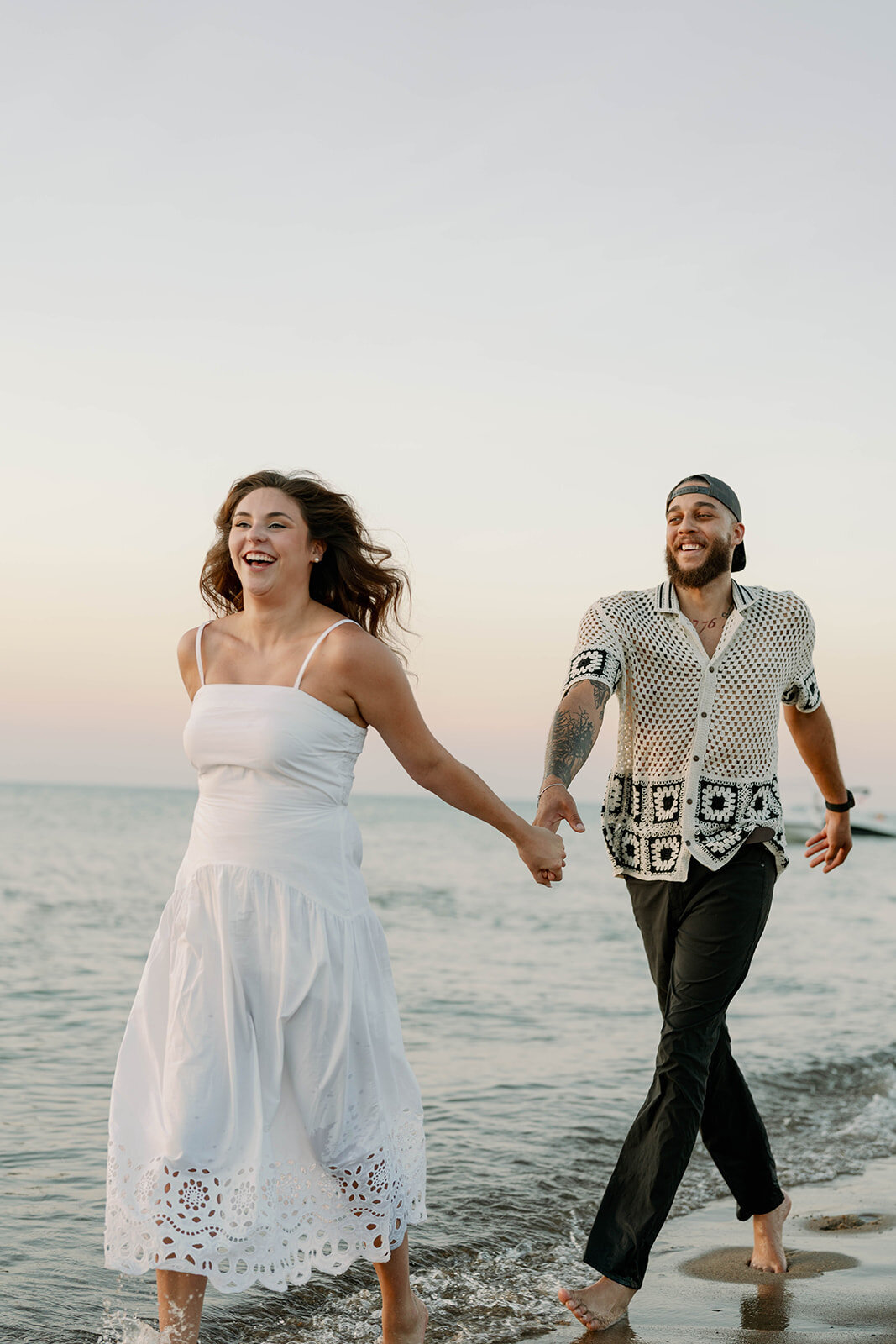 Playful photo of engaged couple running into Lake Michigan waves during sunset engagement photos