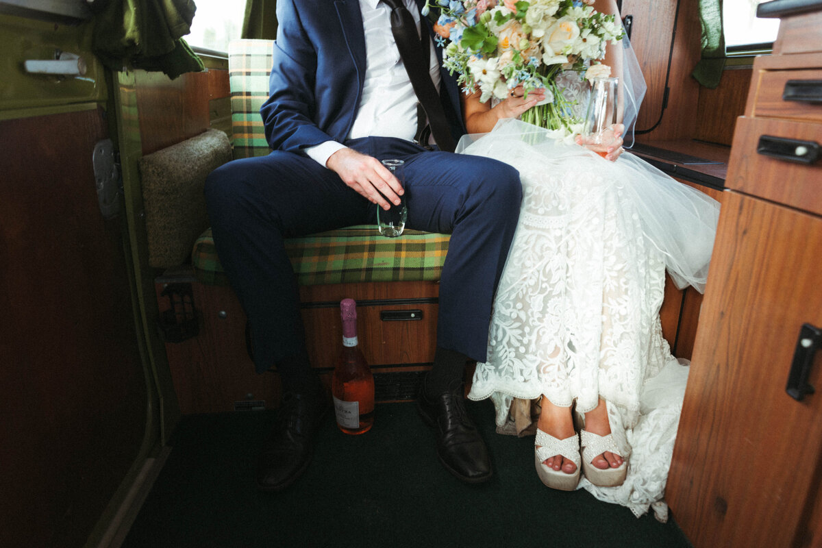 Head on view of a Bride and Groom sitting in the back seat of a VW Bus with a bottle of prosecco