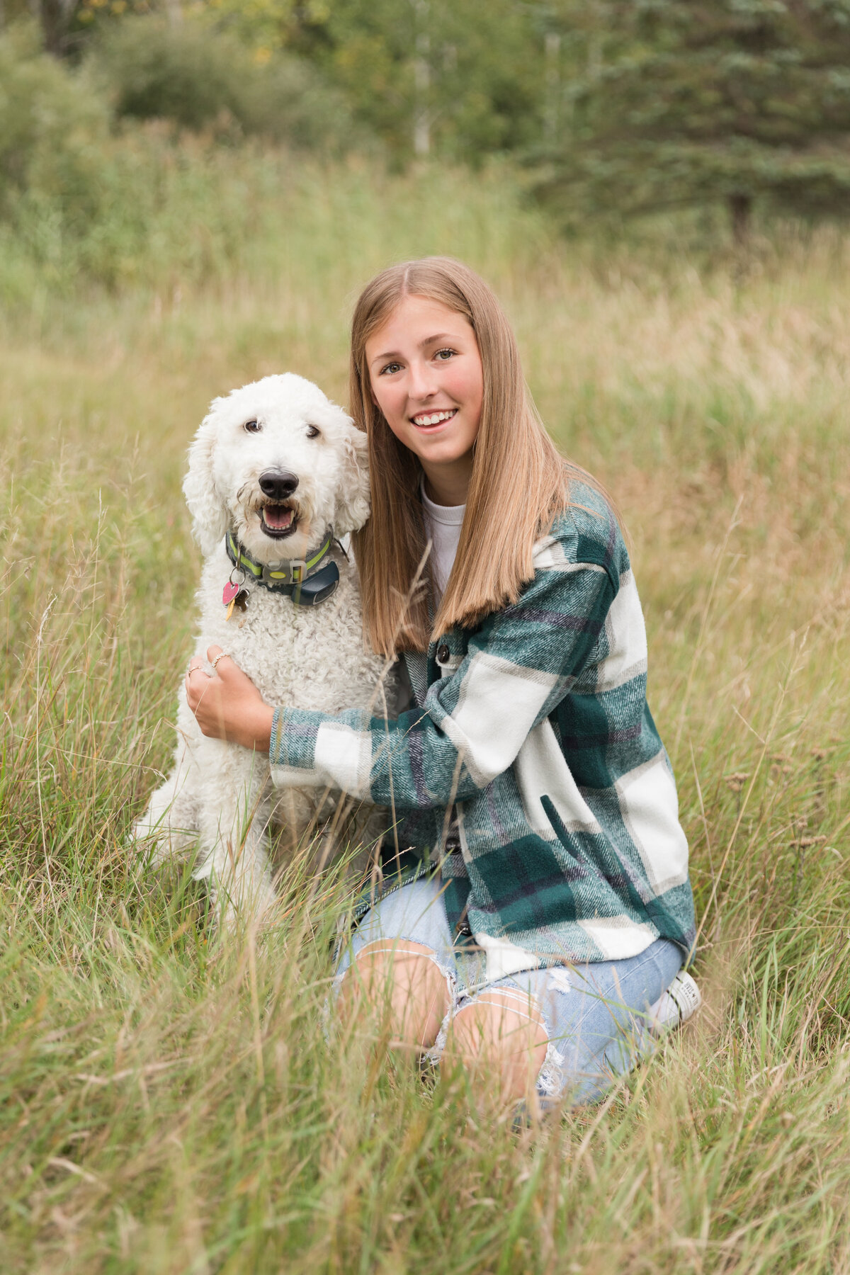 Senior girl seated in a field with her dog smiling at the camera
