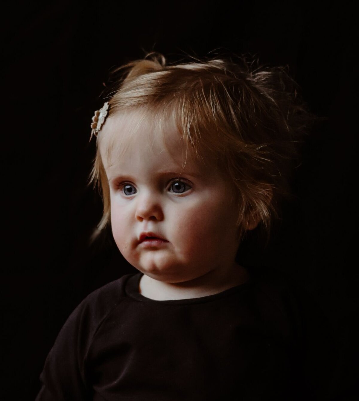 Een portretfoto van een jong meisje met een open en vriendelijke uitstraling, gefotografeerd tegen een donkere achtergrond