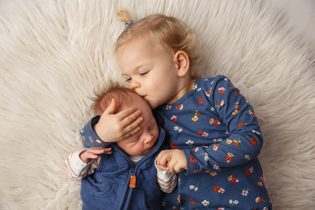 Portrait of a 3 year old girl and her newborn baby brother laying on a rug