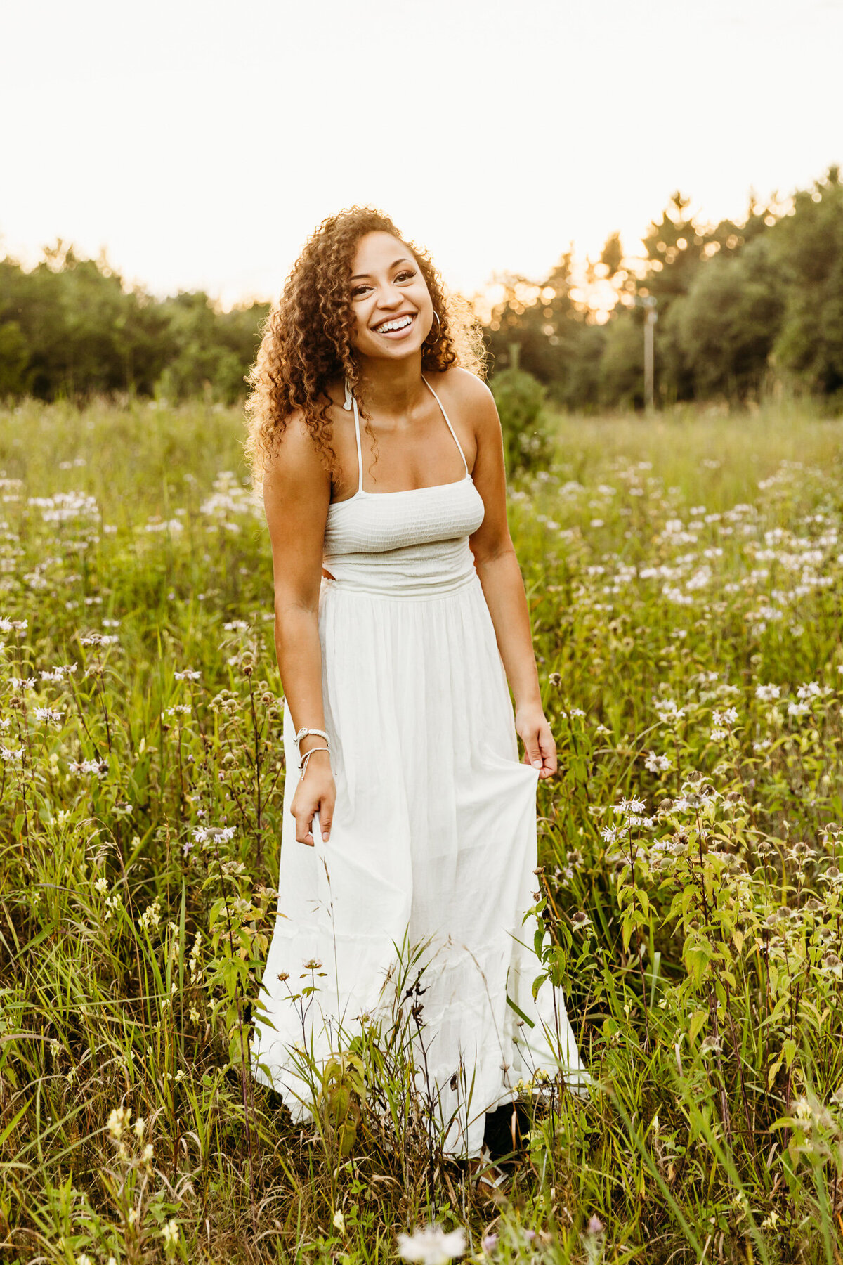 girl in a white dress laughing in a field of wildflowers as the sun sets