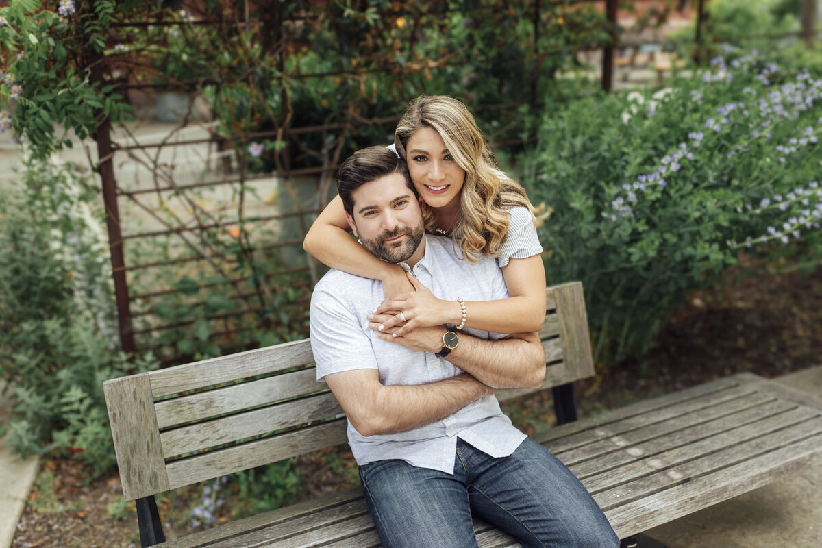 Couple sitting on park bench surrounded by flowers during engagement shoot in Philadelphia Pennsylvania