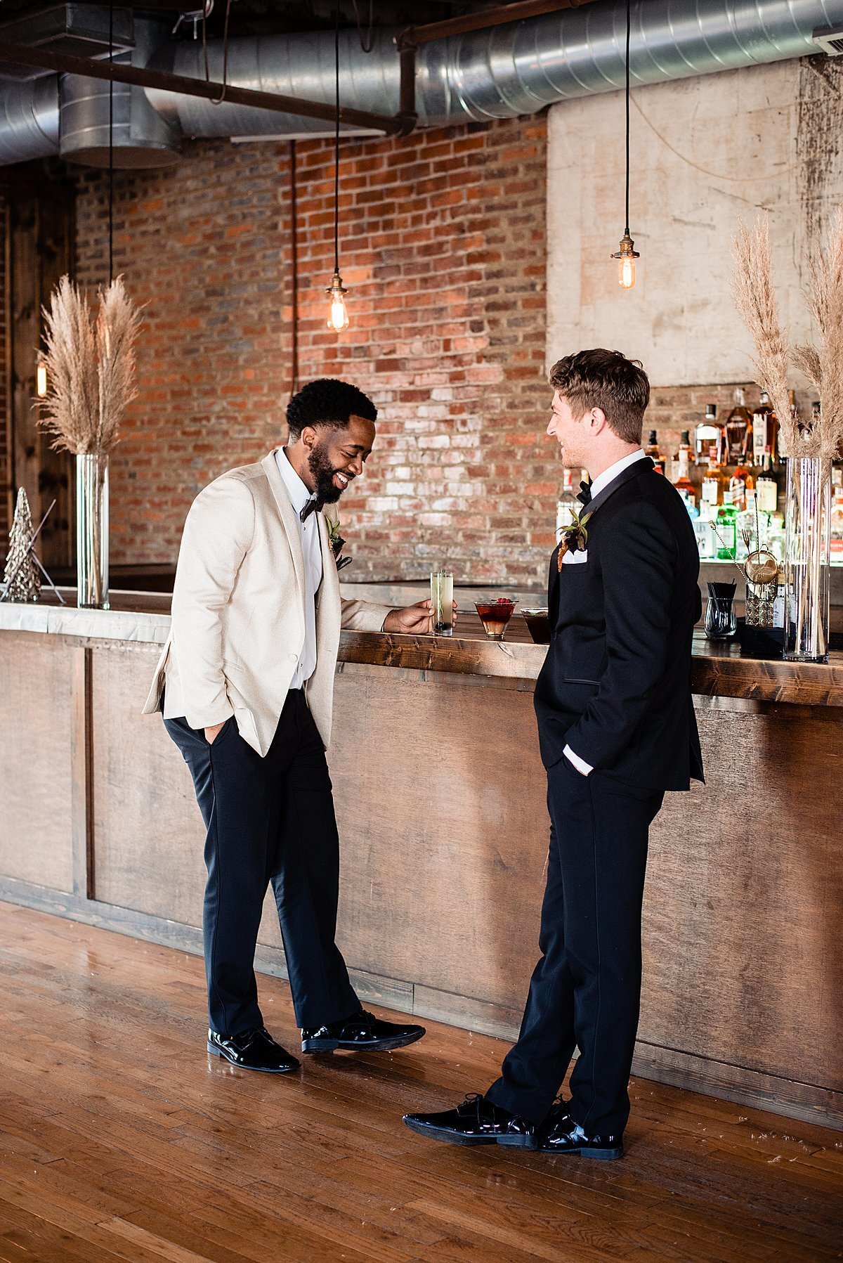 Groom sharing cocktails and chatting with groomsman at the bar inside of Cannery ONE
