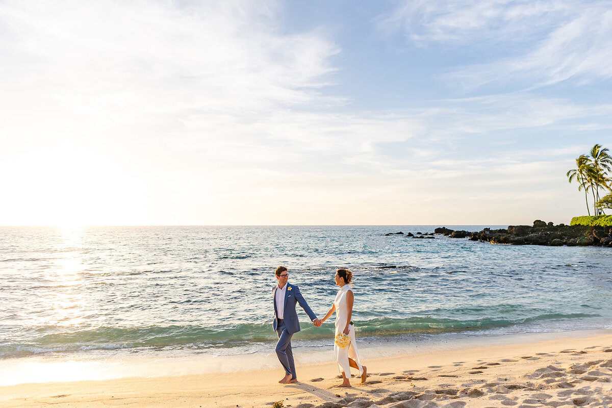 bride and groom walking on white sand beach at sunset