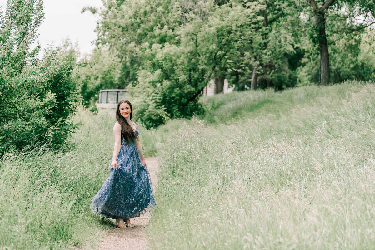 A young lady spinning on a dirt pathholding her dress to the side. 