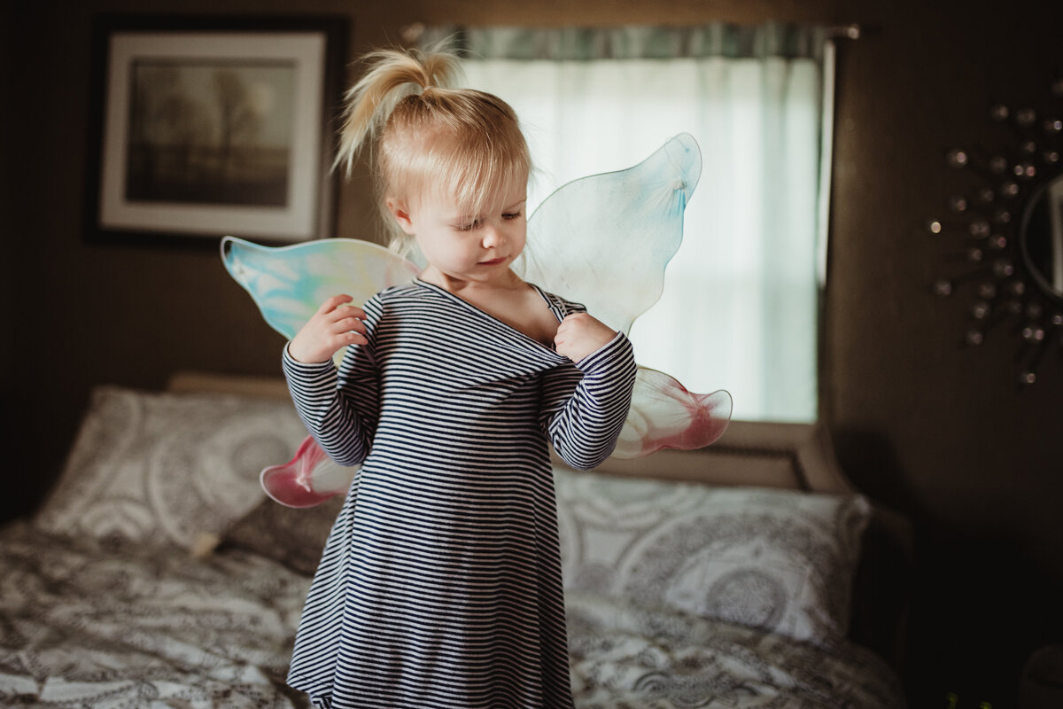 A little girl wearing a striped dress puts on her fairy wings.
